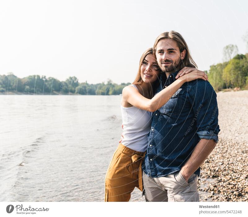 Glückliches junges verliebtes Paar umarmt sich am Flussufer Fluesse Fluß Flüsse glücklich glücklich sein glücklichsein Pärchen Paare Partnerschaft umarmen