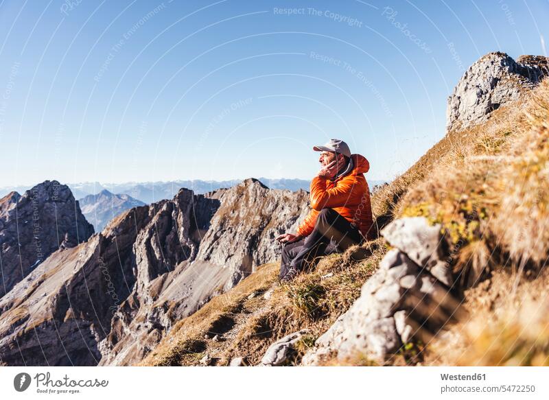 Männlicher Wanderer nachdenklich, während er auf einem Berg gegen den klaren Himmel an einem sonnigen Tag sitzt Farbaufnahme Farbe Farbfoto Farbphoto Österreich