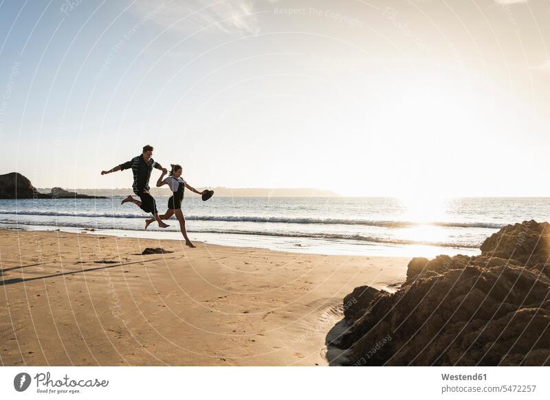 Frankreich, Bretagne, glückliches junges Paar springt bei Sonnenuntergang am Strand Glück glücklich sein glücklichsein Pärchen Paare Partnerschaft springen