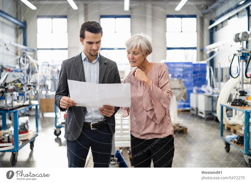 Geschäftsmann und ältere Frau mit Blick auf den Plan in einer Fabrik weiblich Frauen Pläne ansehen Seniorin Seniorinnen alt Businessmann Businessmänner