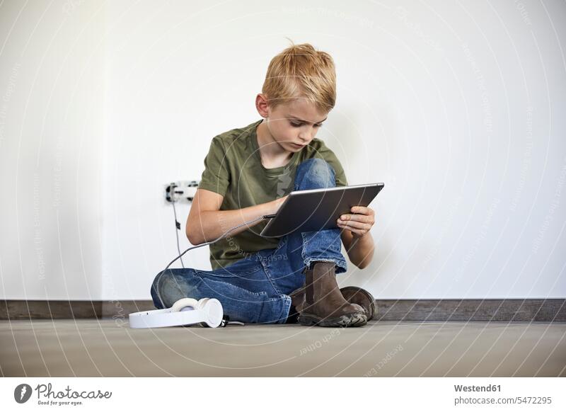 Kleiner Junge spielt auf digitalem Tablet, während er im neuen Haus sitzt Farbaufnahme Farbe Farbfoto Farbphoto Innenaufnahme Innenaufnahmen innen drinnen Tag