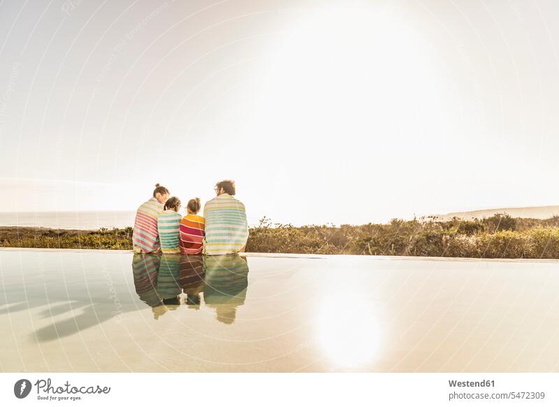 In Handtücher gewickelte Familie sitzt bei Sonnenuntergang am Pool Touristen sitzend Jahreszeiten sommerlich Sommerzeit entspannen relaxen entspanntheit relaxt