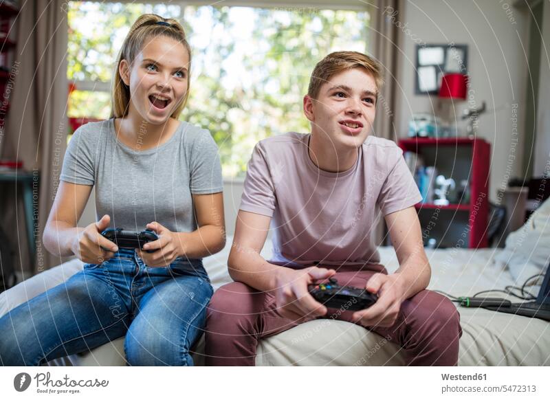 Glückliches Teenager-Mädchen und Junge sitzen im Bett und spielen Videospiel Betten Freunde Videospiele sitzend sitzt zusehen zusehend glücklich glücklich sein