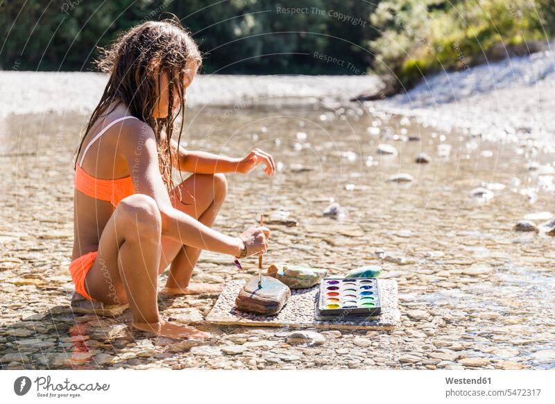Mädchen sitzt im Wasser eines Flusses Malerei auf Stein sitzen sitzend weiblich Steine bemalen anmalen Fluesse Fluß Flüsse Kind Kinder Kids Mensch Menschen