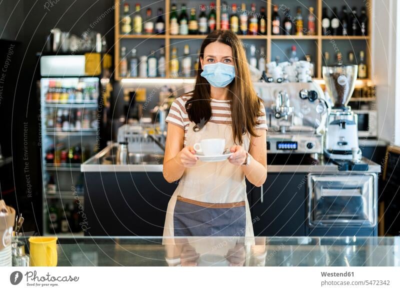 Schöner Besitzer trägt Maske, während er Kaffeetasse und Untertasse im Café hält Farbaufnahme Farbe Farbfoto Farbphoto Innenaufnahme Innenaufnahmen innen