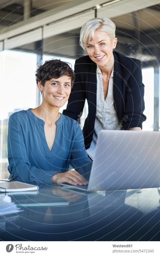 Porträt von zwei lächelnden Geschäftsfrauen mit Laptop am Schreibtisch im Büro Office Büros Businesswomen Businessfrauen Businesswoman Kollegin Kolleginnen