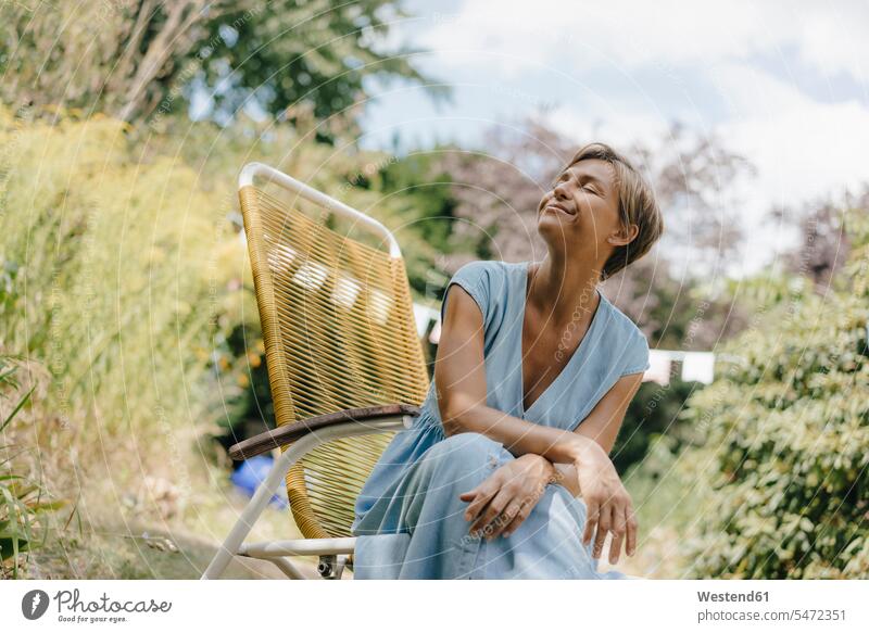 Entspannte Frau sitzt im Garten auf einem Stuhl mit geschlossenen Augen entspannt entspanntheit relaxt sitzen sitzend Stuehle Stühle weiblich Frauen Gärten