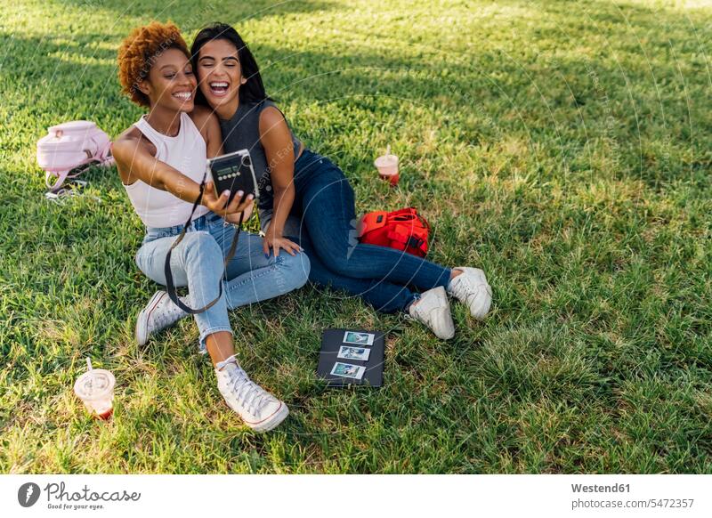 Zwei glückliche Freundinnen machen ein Sofortfoto in einem Park Parkanlagen Parks Glück glücklich sein glücklichsein Sofortbild Polaroids Sofortbilder entspannt
