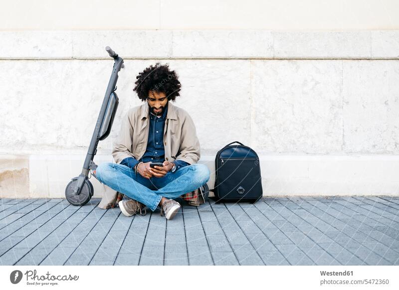 Mann sitzt auf seinem E-Scooter und benutzt ein Mobiltelefon Leute Menschen People Person Personen gemischtrassig 1 Ein ein Mensch nur eine Person single