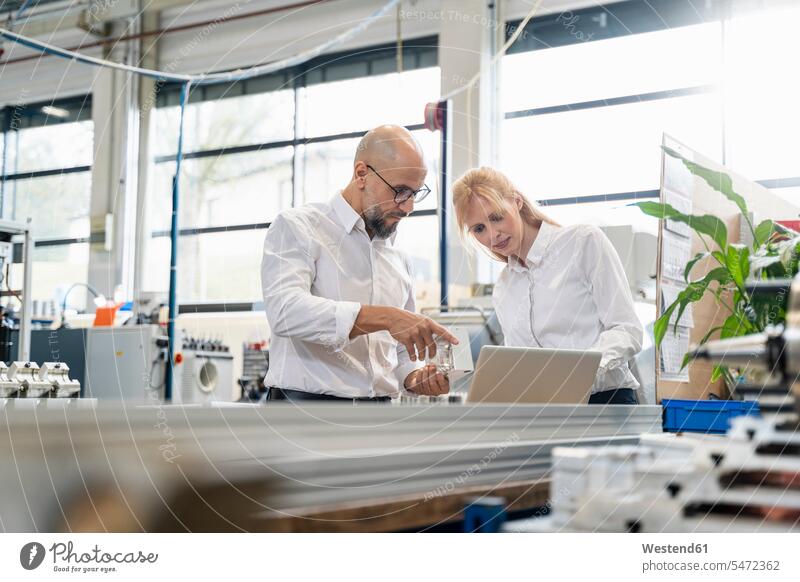 Geschäftsmann und Geschäftsfrau mit Laptop, die ein Werkstück in einer Fabrik untersuchen Notebook Laptops Notebooks prüfen Businessmann Businessmänner