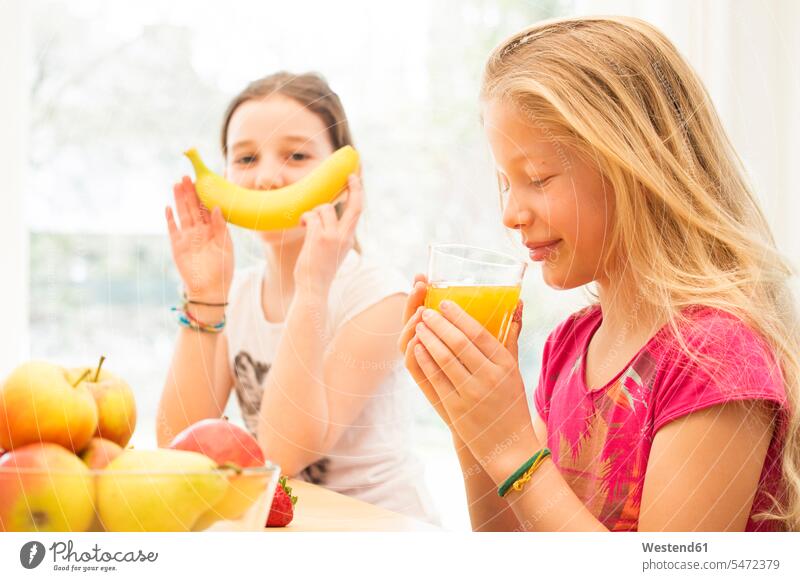 Porträt eines Mädchens, das ein Glas Orangensaft trinkt, während ihre Freundin sich mit einer Banane vergnügt Apfelsinen Bananen Apfelsinensaft O-Saft Spaß