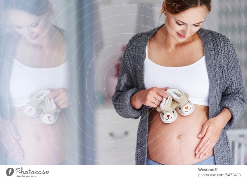 Schwangere Frau mit Babyschuhen lächeln weiblich Frauen Portrait Porträts Portraits Kinderzimmer streicheln schwanger schwangere Frau Zuhause zu Hause daheim