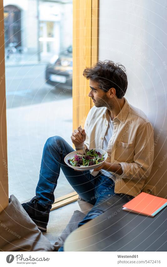 Mann isst einen Salat und sitzt in einem Restaurant am Fenster und schaut hinaus Leute Menschen People Person Personen Alleinstehende Alleinstehender Singles