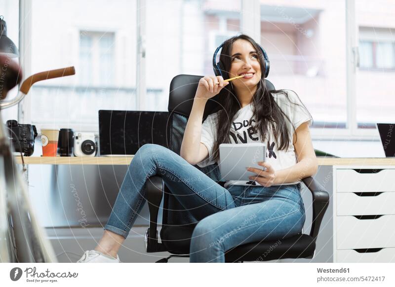 Lässige junge Frau mit Notizblock und Kopfhörern im Coworking Space Notizbloecke Notizblöcke Kopfhoerer weiblich Frauen Büro Office Büros lächeln Erwachsener