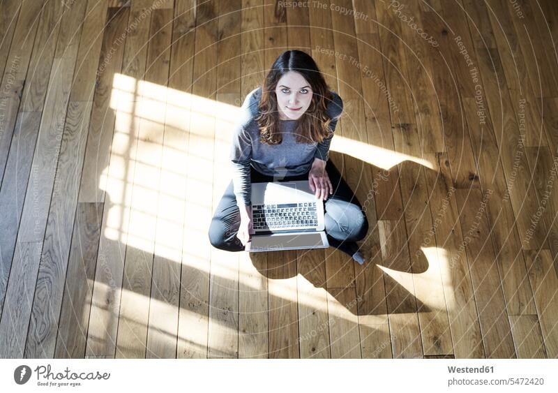 Porträt einer jungen Frau mit Laptop auf Holzboden weiblich Frauen Notebook Laptops Notebooks Holzboeden Holzböden Portrait Porträts Portraits Erwachsener