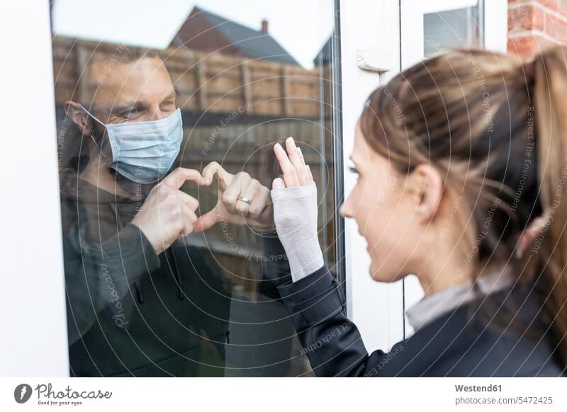 Freund zeigt herzförmige Geste gegenüber seiner Freundin durch Fensterglas, während er zu Hause unter Quarantäne steht Farbaufnahme Farbe Farbfoto Farbphoto Tag
