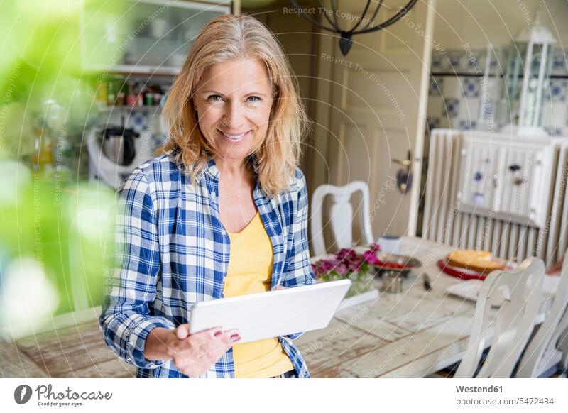 Porträt einer lächelnden reifen Frau mit digitalem Tablet in der Küche Tische Esstische Holztische daheim zu Hause Muße Lifestyles Anschluss verbinden verbunden