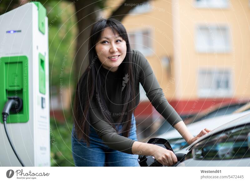 Carsharing, Frau lädt ein Elektroauto auf freuen Glück glücklich sein glücklichsein zufrieden mobil Travel außen draußen im Freien Portraits Porträt Porträts