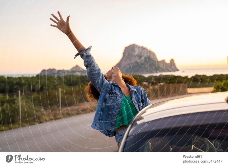 Junge Frau während einer Autofahrt mit erhobenem Arm KFZ Verkehrsmittel Automobil Autos PKW PKWs Wagen sitzend sitzt abends freuen geniessen Genuss Glück