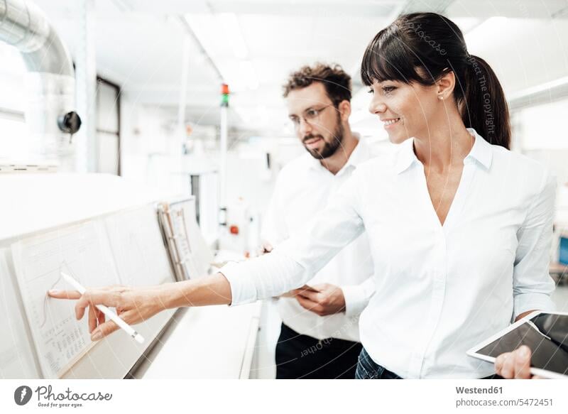 Lächelnde Technikerin zeigt auf Grafik, während sie mit einem männlichen Kollegen im Labor diskutiert Farbaufnahme Farbe Farbfoto Farbphoto Deutschland