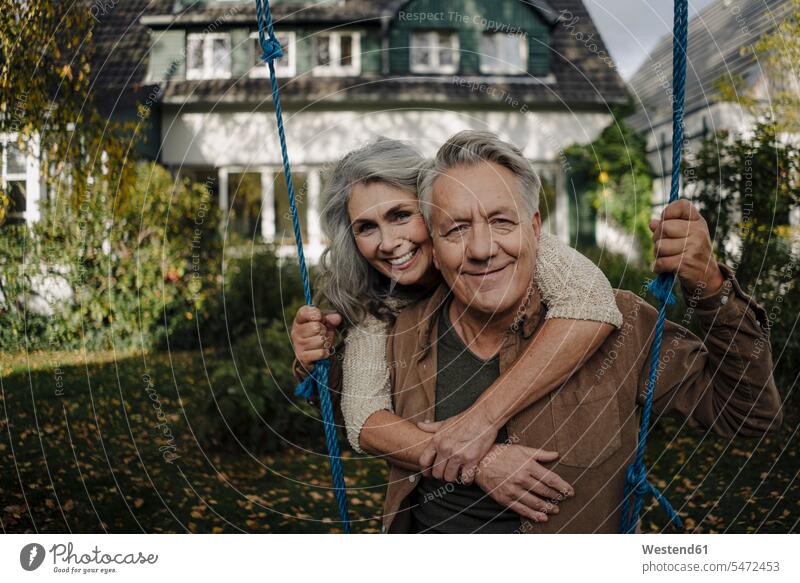 Porträt einer glücklichen Frau, die einen älteren Mann auf einer Schaukel im Garten umarmt Leute Menschen People Person Personen Europäisch Kaukasier kaukasisch