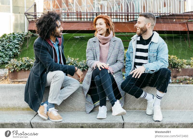 Drei glückliche Freunde, die in der Stadt sitzen und sich unterhalten staedtisch städtisch sitzend sitzt sprechen reden Glück glücklich sein glücklichsein