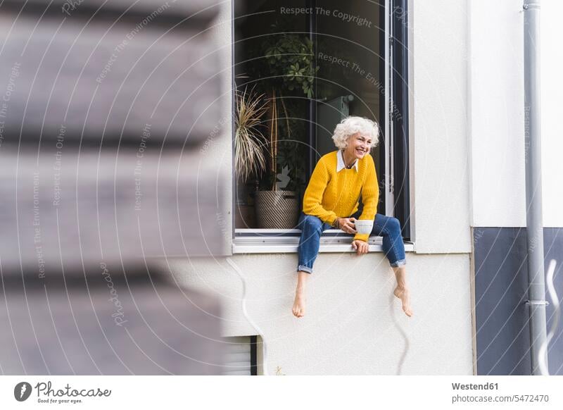 Reife Frau hält Kaffeetasse, während sie am Fenster sitzt Farbaufnahme Farbe Farbfoto Farbphoto Außenaufnahme außen draußen im Freien Tag Tageslichtaufnahme