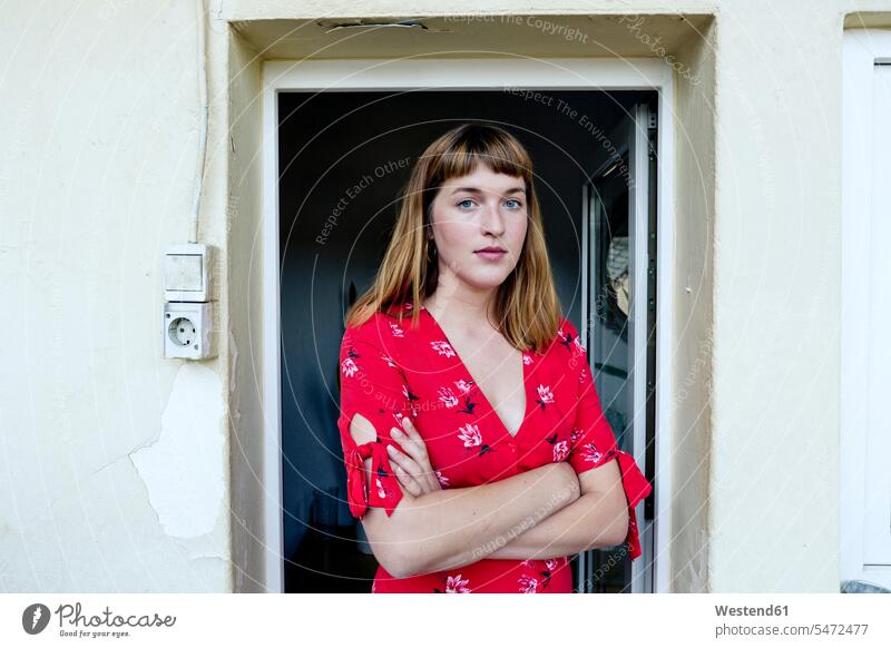 Porträt einer ernsten jungen Frau mit verschränkten Armen, die vor einer geöffneten Balkontür steht Leute Menschen People Person Personen Europäisch Kaukasier