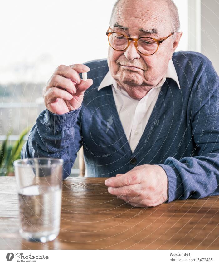 Porträt eines älteren Mannes am Tisch sitzend mit Pille und Glas Wasser Senior ältere Männer älterer Mann Senioren Portrait Porträts Portraits sitzt Tablette