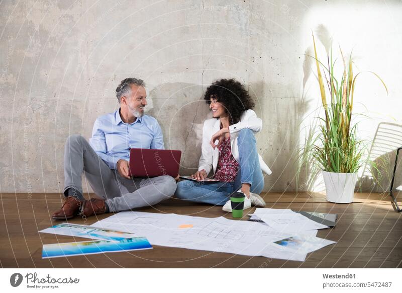 Geschäftsmann und Geschäftsfrau sitzen auf dem Boden in einem Loft arbeiten mit Laptop und Dokumente Notebook Laptops Notebooks Unterlagen sitzend sitzt Böden