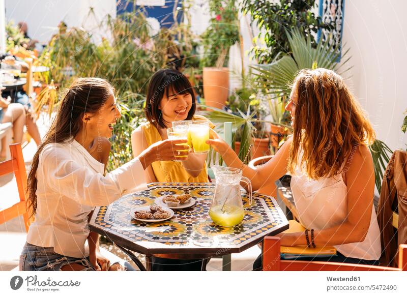 Drei glückliche Freundinnen treffen sich in einem Café mit klirrenden Limonadengläsern Leute Menschen People Person Personen Europäisch Kaukasier kaukasisch