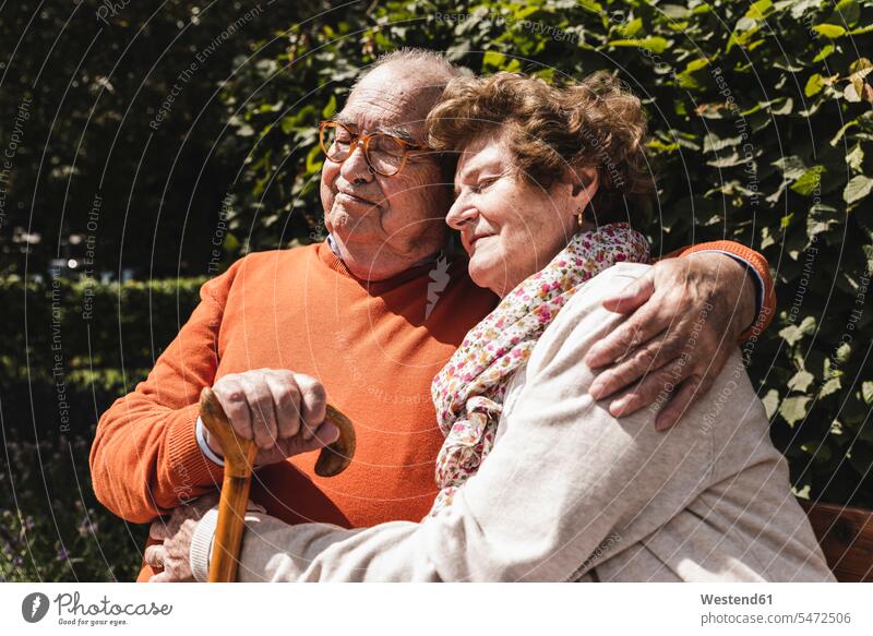 Älteres Paar sitzt auf einer Bank in einem Park, mit den Armen um Parkanlagen Parks Sommer Sommerzeit sommerlich Seniorenpaar älteres Paar Seniorenpaare