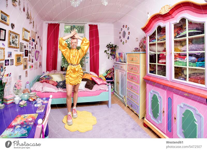 Junge Frau mit erhobener Hand und herausgestreckter Zunge im Schlafzimmer stehend Farbaufnahme Farbe Farbfoto Farbphoto Innenaufnahme Innenaufnahmen innen