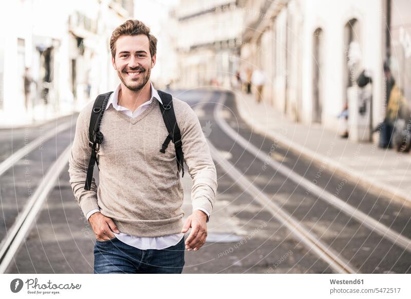Porträt eines lächelnden jungen Mannes mit Rucksack in der Stadt unterwegs, Lissabon, Portugal Touristen Rucksäcke gehend geht freuen geniessen Genuss zufrieden