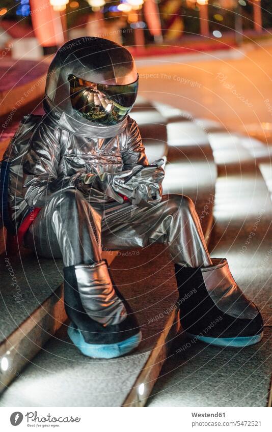 Raumfahrer, der nachts auf einer beleuchteten Treppe sitzt und ein Mobiltelefon benutzt Astronaut Astronauten Weltraumfahrer Beleuchtung Handy Handies Handys
