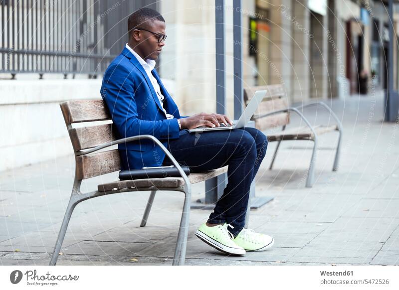 Junger Geschäftsmann in blauer Anzugjacke sitzt auf Bank und benutzt Laptop Job Berufe Berufstätigkeit Beschäftigung Jobs geschäftlich Geschäftsleben