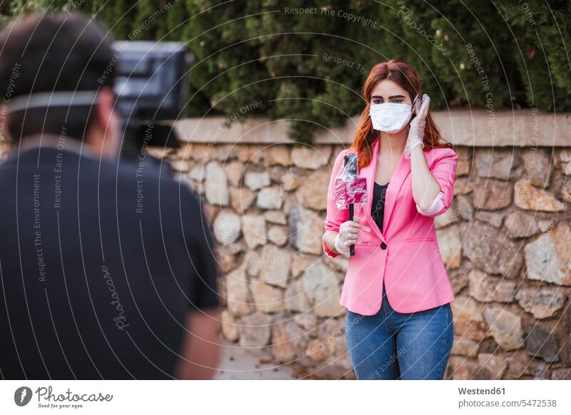 Kameramann filmt Reporter mit Mikrofon, der eine Maske trägt, während er an der Wand steht Farbaufnahme Farbe Farbfoto Farbphoto Spanien Tag Tageslichtaufnahme