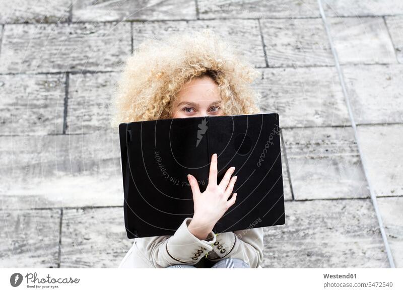Blonde Frau mit Locken versteckt sich hinter schwarzem Ordner Mappe Mappen schwarzer schwarzen schwarzes weiblich Frauen Ringellocke Ringellocken blond