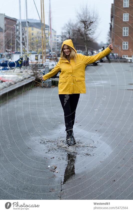 Dänemark, Kopenhagen, glückliche Frau springt in Pfützen am Stadthafen staedtisch städtisch weiblich Frauen Glück glücklich sein glücklichsein Lache springen