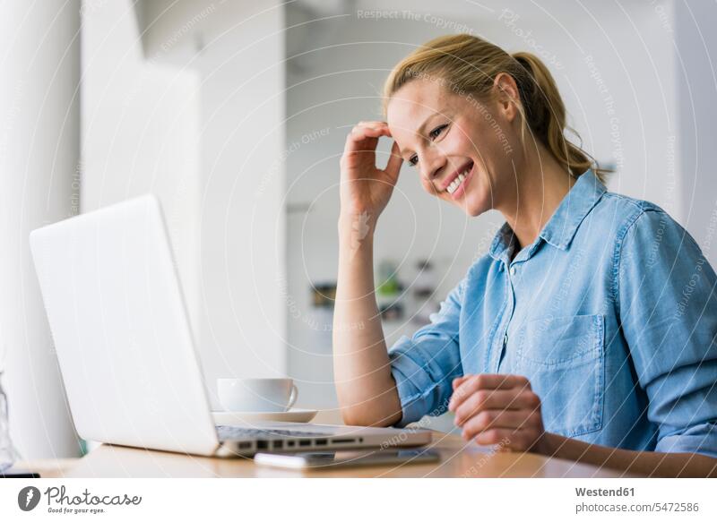 Blonde Frau sitzt im Café und benutzt einen Laptop Rechner Laptops Notebook Notebooks Arbeit sitzend freuen Glück glücklich sein glücklichsein zufrieden