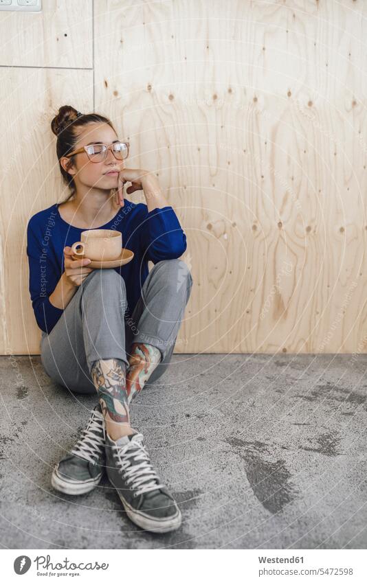 Junge Frau, die eine Pause im Büro macht und Kaffee aus einer Holztasse trinkt auf dem Boden sitzen auf dem Boden sitzend hoelzern hölzern Pause machen
