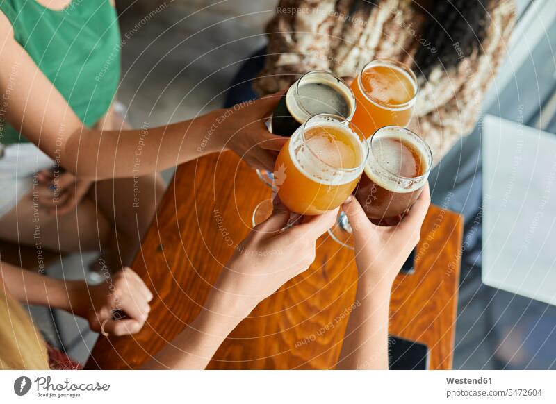 Freundinnen, die in einer Kneipe mit handwerklichen Biergläsern klimpern Freunde Kameradschaft Gläser Trinkglas Trinkgläser Tische Holztische sitzend sitzt