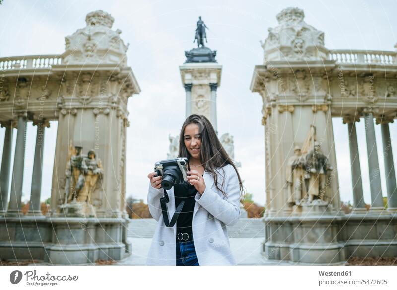 Lächelnde Frau mit einer Kamera vor dem Alfonso-XII-Denkmal im Park El Retiro, Madrid, Spanien Touristen Fotokamera freuen Frohsinn Fröhlichkeit Heiterkeit