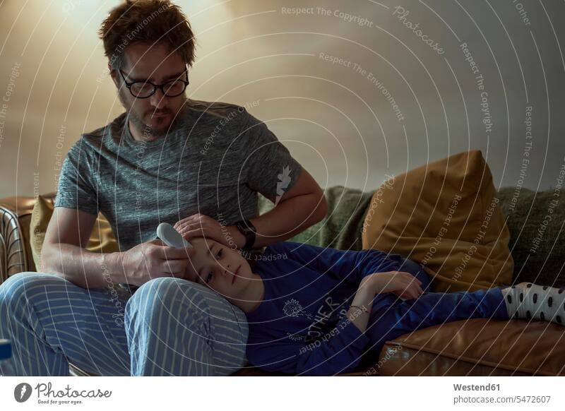 Mann hält Thermometer auf der Stirn der kranken Tochter im Wohnzimmer zu Hause Farbaufnahme Farbe Farbfoto Farbphoto Innenausstattung Wohnraum