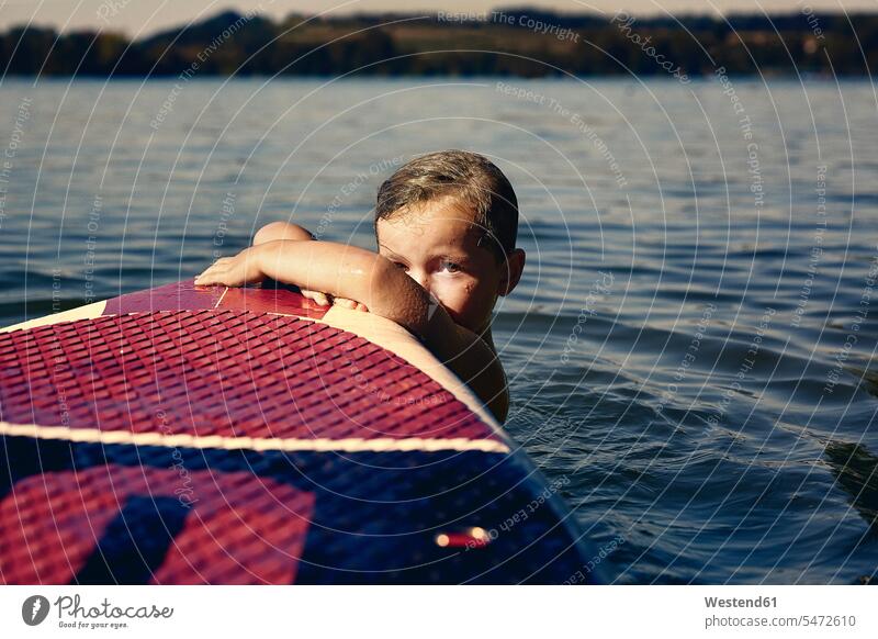 Junge mit SUP-Tafel auf einem See in der Abenddämmerung abends Jahreszeiten sommerlich Sommerzeit Naesse Nässe Muße Spass spassig spaßig Spässe Späße Travel