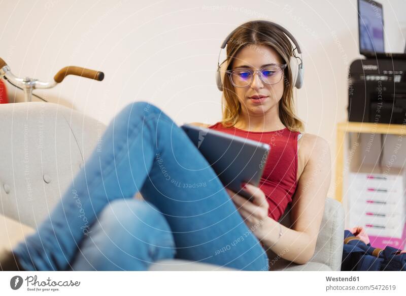 Lässige junge Frau mit Kopfhörern, die ein Tablet im Coworking Space benutzt Büro Office Büros Kopfhoerer weiblich Frauen Tablet Computer Tablet-PC Tablet PC