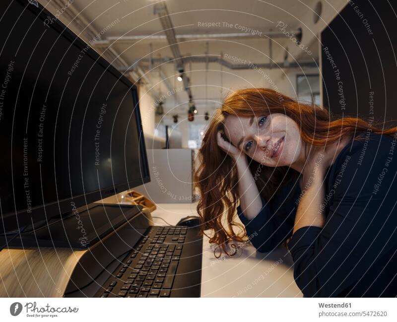 Porträt einer lächelnden rothaarigen Frau, die im Büro am Schreibtisch sitzt Leute Menschen People Person Personen Europäisch Kaukasier kaukasisch 1 Ein
