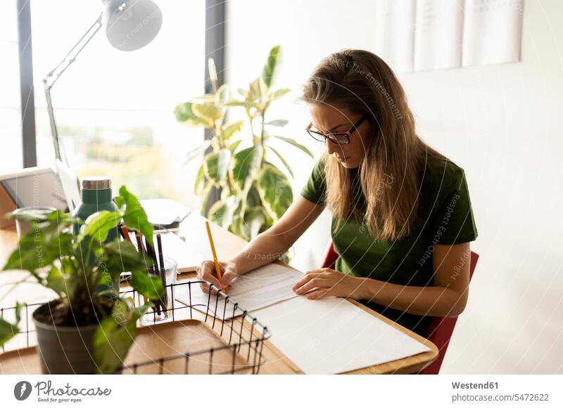 Geschäftsfrau schreibt auf Papier, während sie im Home-Office sitzt Farbaufnahme Farbe Farbfoto Farbphoto Spanien Freizeitkleidung Freizeitbekleidung casual