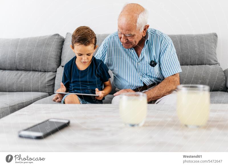 Großvater und Enkel sitzen zusammen auf der Couch zu Hause und schauen auf ein digitales Tablet Gemeinsam Zusammen Miteinander Tablet Computer Tablet-PC