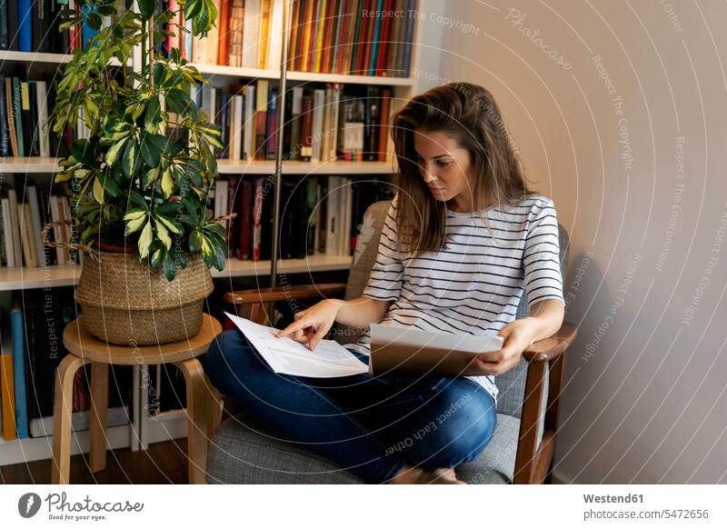 Geschäftsfrau liest Dokument, während sie im Home-Office auf einem Stuhl sitzt Farbaufnahme Farbe Farbfoto Farbphoto Spanien Freizeitkleidung Freizeitbekleidung